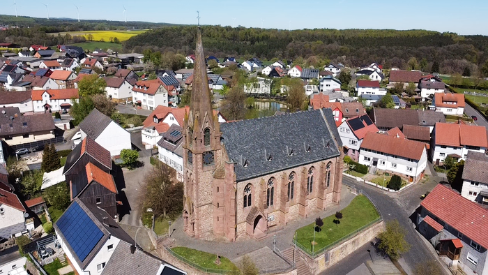 Luftaufnahme eines malerischen Dorfes mit einer markanten historischen Kirche, umgeben von Wohnhäusern.