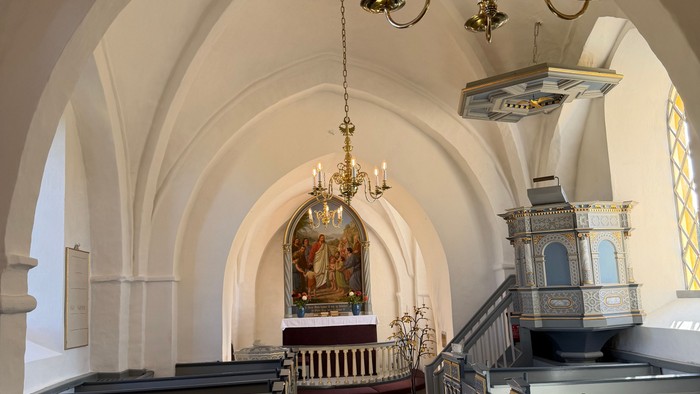 Elegant kirkeinteriør med hvælvede lofter, kirkebænke og prægtige lysekroner, der oplyser alterområdet.