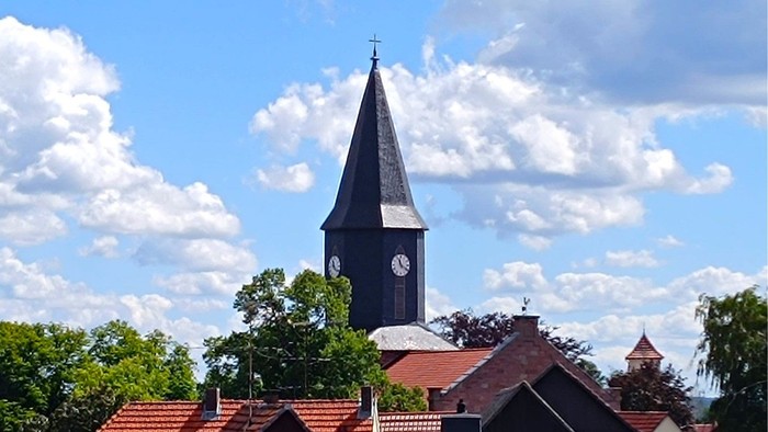 Kirchturm mit Uhrwerk vor blauem Himmel und weißen Wolken
