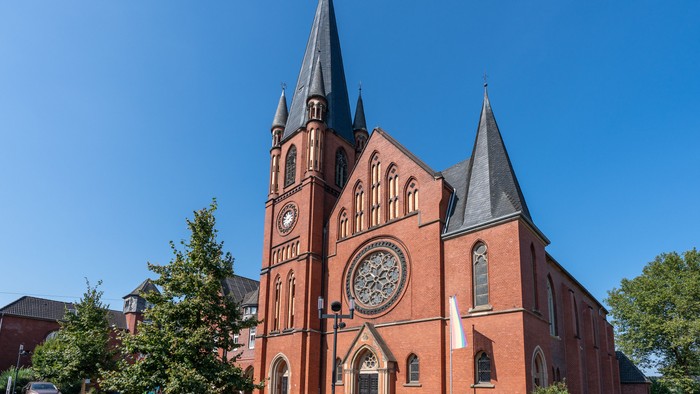 Imposante Backsteinkirche mit Zwillingstürmen und einer markanten Uhr unter klarem blauem Himmel.