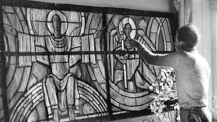 Eine Person reinigt oder bearbeitet sorgfältig ein kunstvolles Kirchenfenster mit religiösen Motiven.