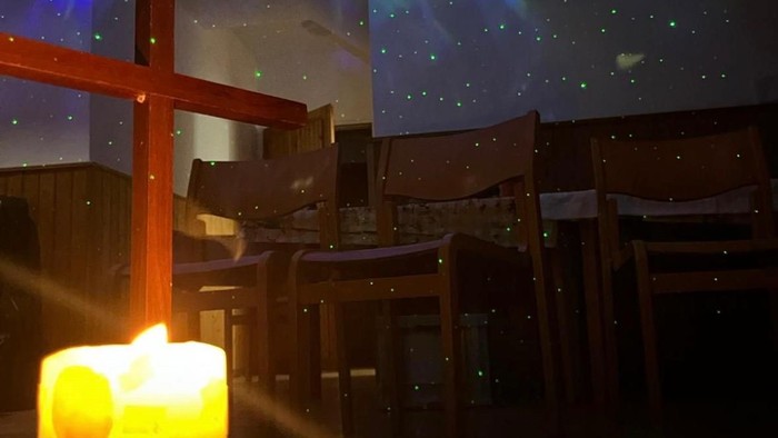 Ein gemütlicher Innenbereich zum Essen mit einer Sternenhimmel-Projektion und einer brennenden Adventskerze auf dem Tisch.