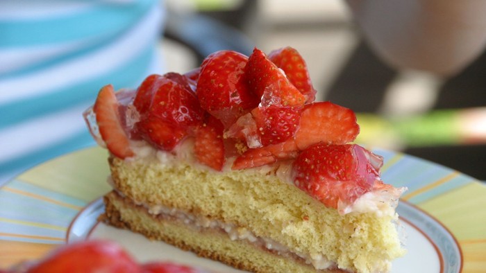 Ein Stück Schichtkuchen mit frischen Erdbeeren und Schlagsahne auf einem dekorativen Teller.