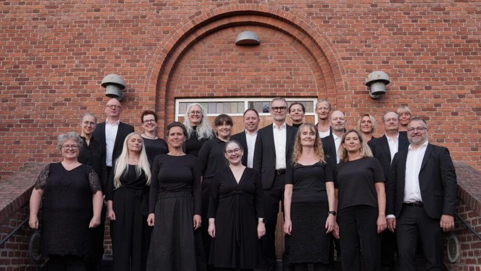 En formel korgruppe, der poser sammen foran en murstensbygning med en buet indgang.