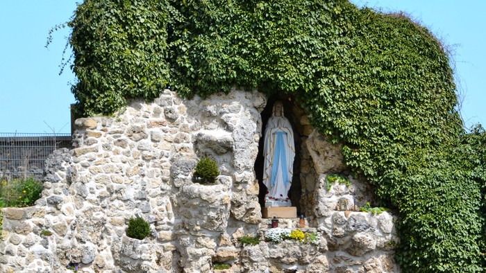 Ein mit Efeu bewachsener Steinschrein, in dem eine Statue der Jungfrau Maria mit Blumenopfern steht.