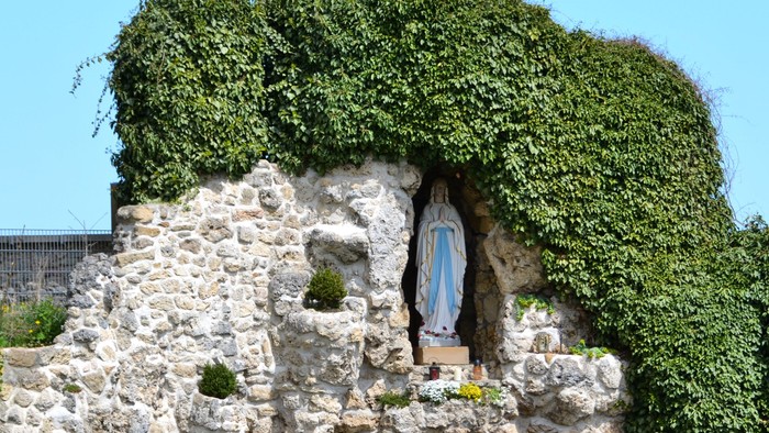 Ein mit Efeu bewachsener Steinschrein, in dem eine Statue der Jungfrau Maria mit Blumenopfern steht.