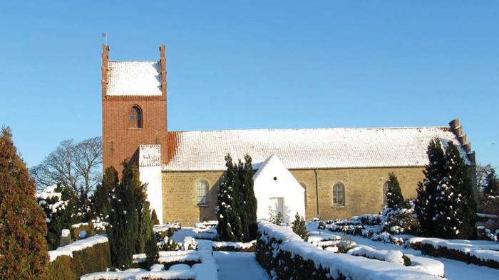 En snede kirke med tårn og hvide vinduer, omgivet af sne og træer