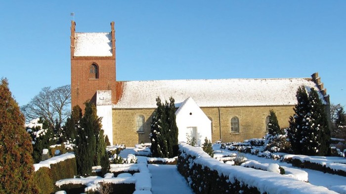 En snede kirke med tårn og hvide vinduer, omgivet af sne og træer