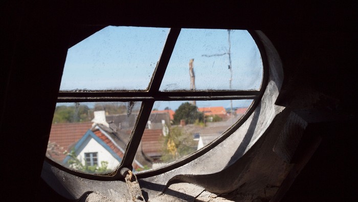 Et vindueskarm med skader og udsigt over en landsby.