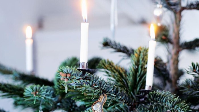 Tændt hvidt levende lys på grangren på juletræ