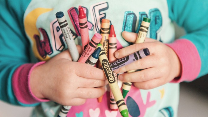 Child holding a variety of colorful crayons.