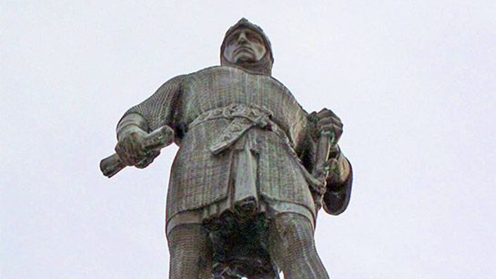 Bronzestatue eines gepanzerten Kriegers, der auf einer verzierten Säule steht.