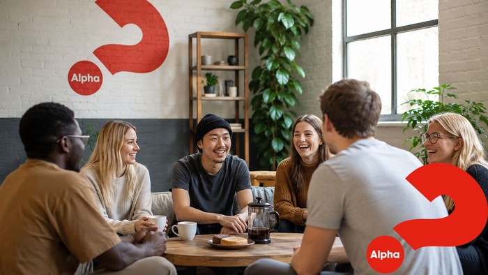 Eine vielfältige Gruppe von Menschen versammelte sich fröhlich um einen Tisch in einem gemütlichen Café mit Alpha-Branding.