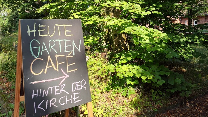 Eine Tafel im Grünen mit Hinweistext: Heute Gartencafé hinter der Kirche