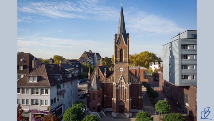 Luftaufnahme einer historischen Kirche mit hohem Turm in einer malerischen europäischen Stadt, umgeben von modernen Gebäuden.