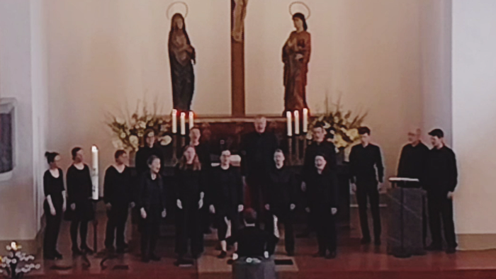 Ein Kirchenchor singt vor einem Kruzifix mit Marienstatue.