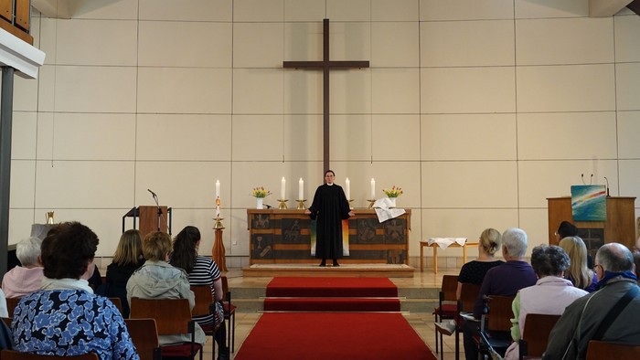 Eine ehrfürchtige Gottesdienstfeier mit einem Priester, der zu einer aufmerksamen Gemeinde spricht, die in hölzernen Kirchenbänken sitzt.
