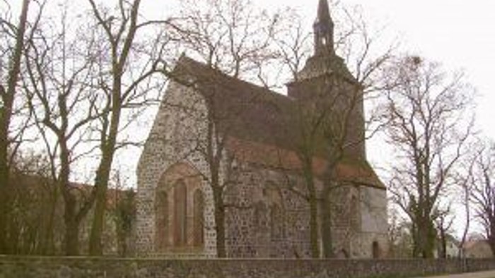 Historische Steinkirche mit hohem Turm, eingebettet zwischen kahlen Winterbäumen und einer Steinmauer.