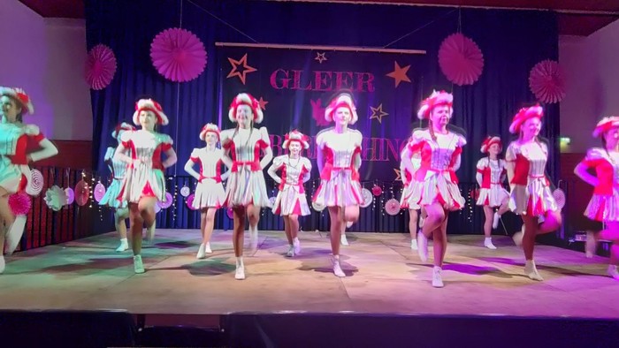 Eine Cheerleading-Mannschaft tritt auf der Bühne mit bunten Kostümen und Pompons bei einer „Glee“-inspirierten Veranstaltung auf.