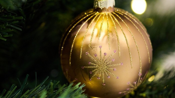 En gylden metallisk julepynt med et stjernemønster, der pryder en pyntet gren på et stedsegrønt juletræ.