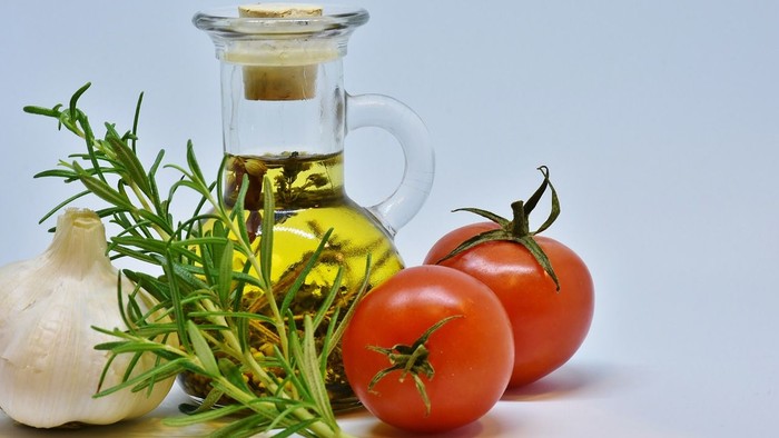 Das Bild zeigt eine Glasflasche mit Öl, Knoblauch, Rosmarin und Tomaten