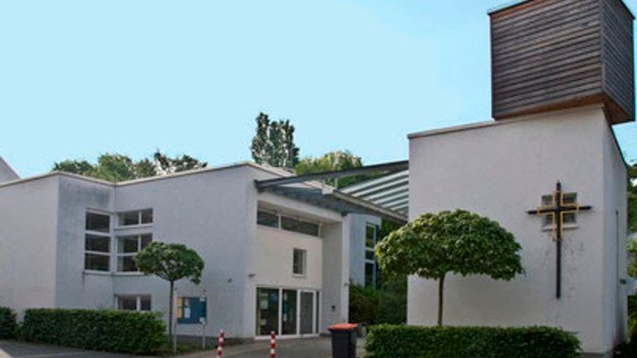 Moderne Kirchengebäude mit weißer Fassade, Kreuz und angrenzendem Wasserturm unter klarem Himmel.