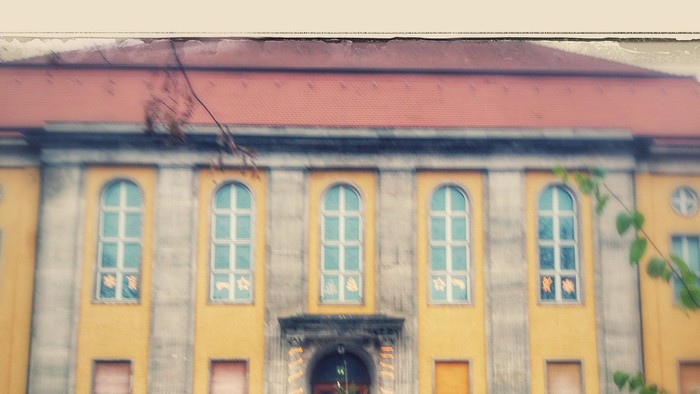 Altbau im Vintage-Stil mit gelb-grauer Fassade, gewölbtem Eingang und Kopfsteinpflasterweg.