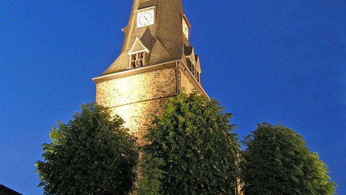Steinkirche mit Uhrturm und Kreuz, umgeben von Bäumen und einer Steinmauer.