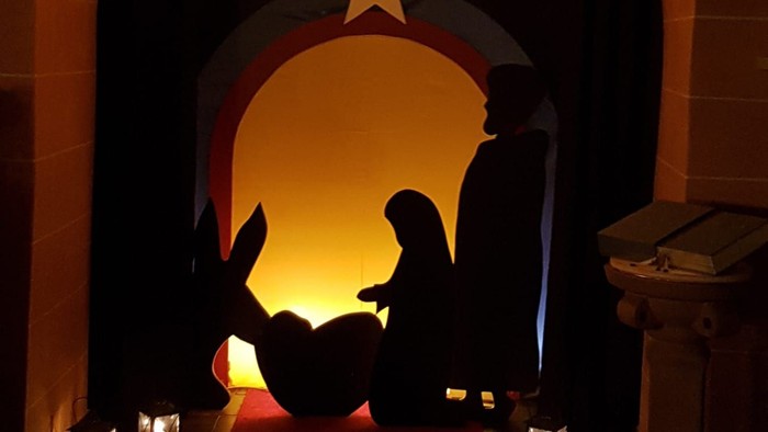 Eine wunderschön beleuchtete Weihnachtskrippe mit einem Stern darüber, Maria, Josef und das Jesuskind als Silhouetten.
