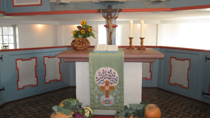 Geschmückter Altar mit Früchten, Kerzen, Blumengesteck und religiösen Symbolen in einer ruhigen Kapelle.