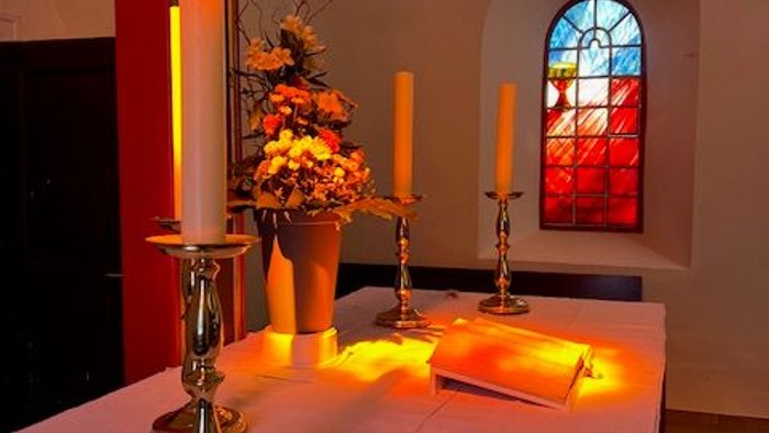 Elegante Tischdekoration mit brennenden Kerzen, Blumenarrangement und einem Buntglasfenster in einer ruhigen Innenraumeinrichtung.