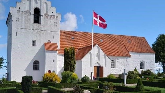 Hvid kirke med rødt tag og dansk flag, omgivet af velplejede haver.