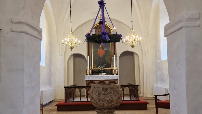 Elegant kirkeinteriør med et alter prydet af lysekroner, dekorative blomster og en stenpiedestal.