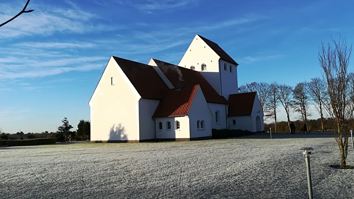 Hvid kirke med sorte tag og klokketårn i åbent landskab