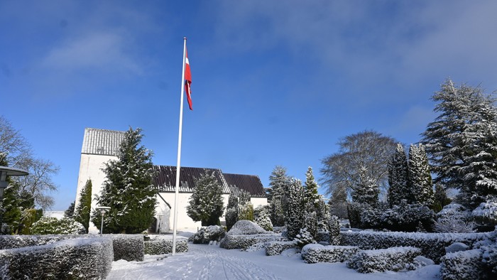 En snedækket park med et hus og en flagstang med rødt flag.
