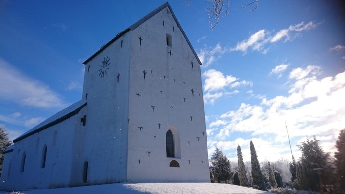 En hvid kirke med kors og solsymboler på fasaden, beliggende i sne og solskin.