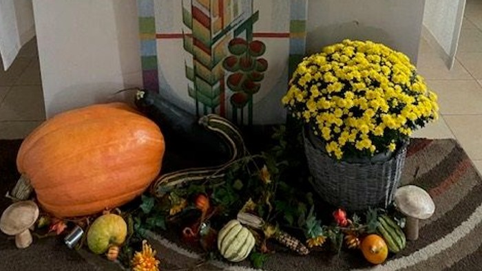 Herbstlich gestalteter Altar mit Erntegaben, Kerzen, Blumen und einem Kruzifix auf einem dekorierten Tisch.