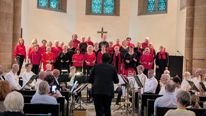 Ein Chor und ein Orchester treten gemeinsam in einer Kirche auf, dirigiert von einem Dirigenten vor sitzendem Publikum.