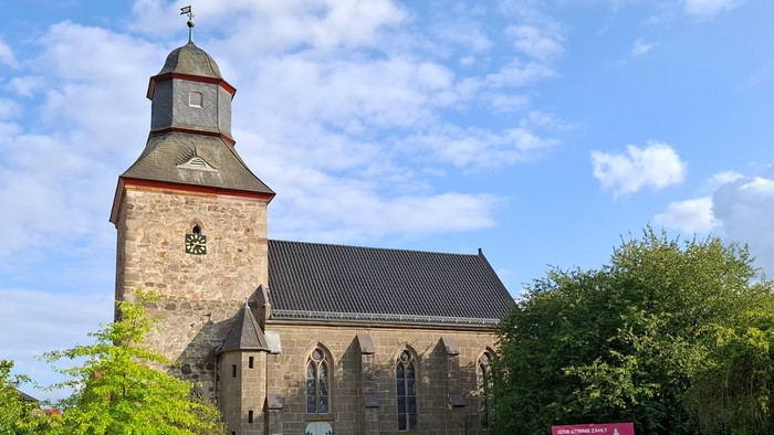 Historische Steinkirche mit hohem Glockenturm in einer üppigen, grünen Landschaft.
