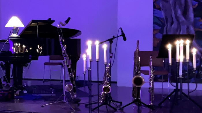 En mørk scene med uddannede blæserinstrumenter og en piano ved lyset af candelabre.