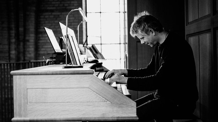 En fokuseret musiker spiller på orglet i en rolig, svagt oplyst kirke.