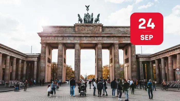 Ikoniske Brandenburger Tor i Berlin med en skare af besøgende og et rødt datostempel med