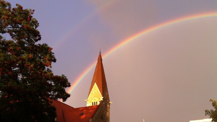 Regnbue over kirke med spiret.