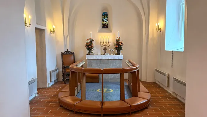 Elegant synagogeinteriør med et cirkulært siddeområde, alter med lys og dekorativt farvet glas.