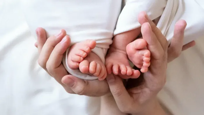 Sanfte Hände, die die Füßchen eines Babys halten, in weißer Kleidung.