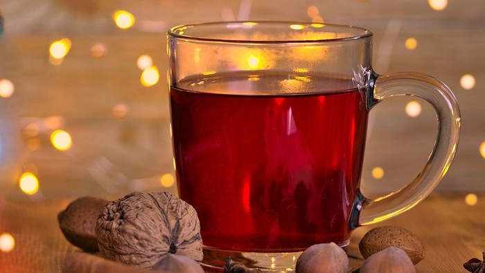 Ein Glas mit heißem Punsch, umgeben von Gewürzen und Kerzenlicht