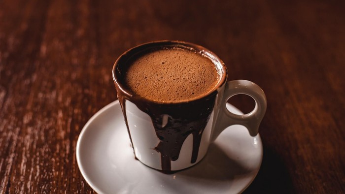 Eine Tasse Kaffee steht auf einem Unterteller auf einem Holztisch.