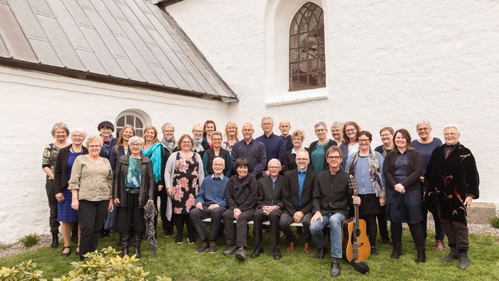 En gruppe af mennesker står sammen udenfor et hvidt kirkebygning