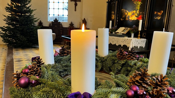En adventskranse med lysede lygter og pynt, placeret i en kirke.