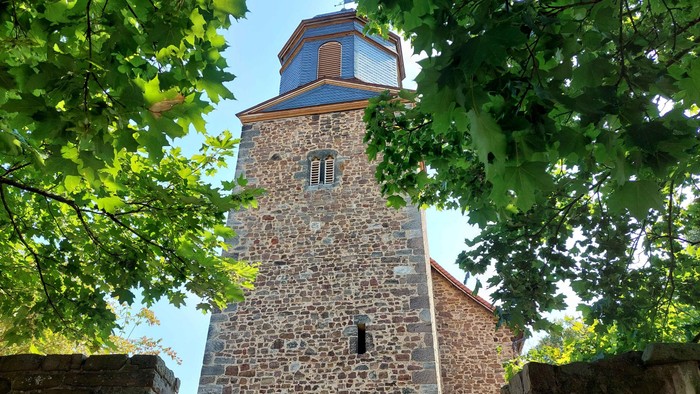 Das Foto zeigt den Kirchturm der Evangelischen Kirche Dörnhagen, umgeben von Bäumen